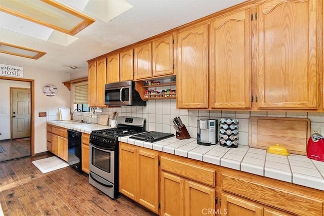 kitchen with appliances with stainless steel finishes, dark wood-type flooring, decorative backsplash, sink, and tile countertops