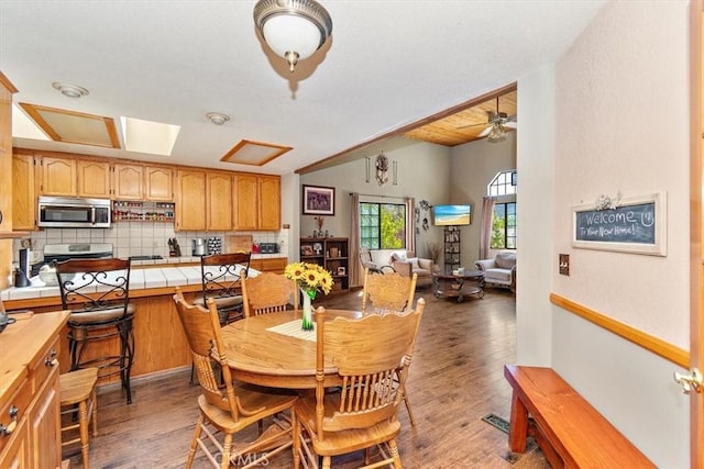 dining area featuring ceiling fan, a skylight, and dark hardwood / wood-style floors