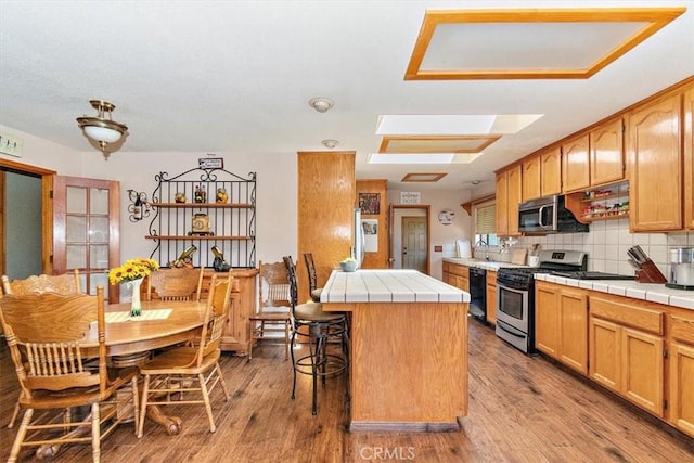 kitchen featuring a skylight, appliances with stainless steel finishes, tile countertops, and a center island