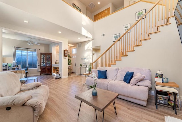 living room featuring ceiling fan, light wood-type flooring, a high ceiling, and a wealth of natural light