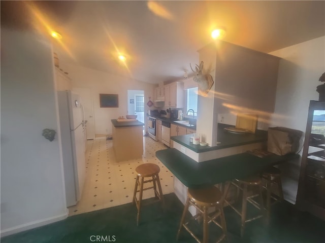 kitchen featuring a breakfast bar, sink, dark tile patterned flooring, white appliances, and white cabinets