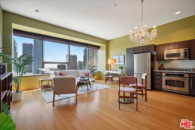 kitchen featuring light wood-type flooring, appliances with stainless steel finishes, dark brown cabinets, and a notable chandelier