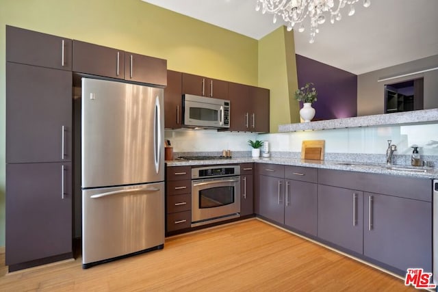 kitchen with appliances with stainless steel finishes, light stone countertops, light hardwood / wood-style floors, a notable chandelier, and sink