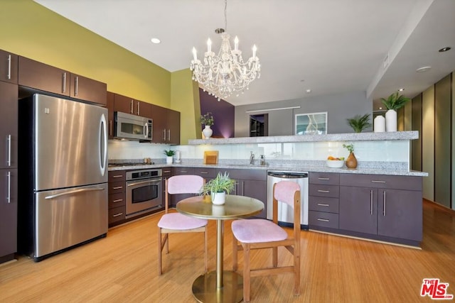 kitchen with dark brown cabinets, a notable chandelier, stainless steel appliances, light stone counters, and light wood-type flooring