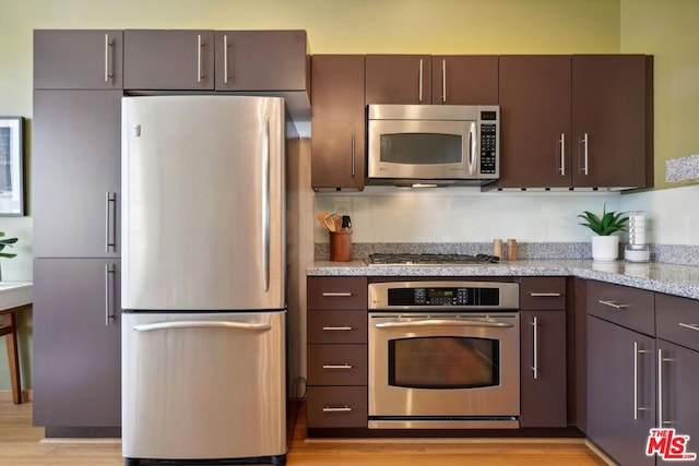 kitchen featuring appliances with stainless steel finishes, dark brown cabinets, light stone countertops, and light hardwood / wood-style floors