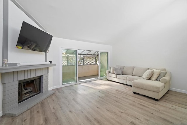 living room featuring vaulted ceiling, light hardwood / wood-style flooring, and a brick fireplace