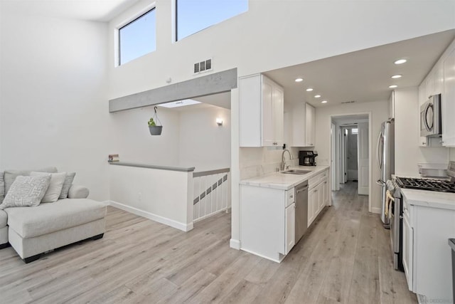 kitchen with appliances with stainless steel finishes, light hardwood / wood-style floors, white cabinetry, sink, and a towering ceiling