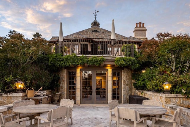 back house at dusk with a patio, french doors, and a balcony