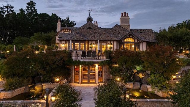 back house at dusk featuring french doors and a balcony