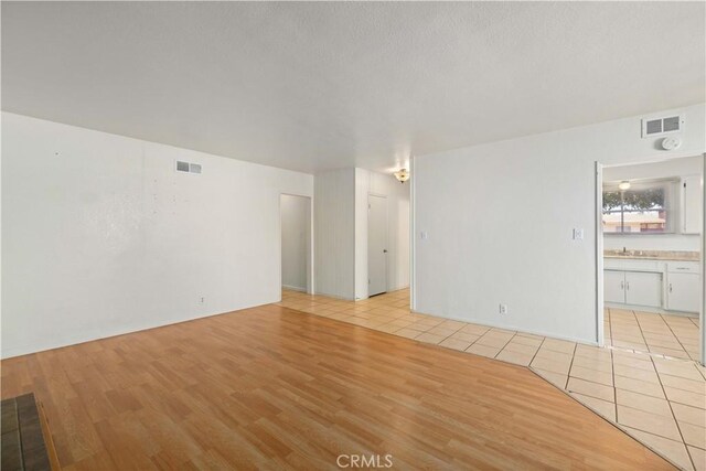 unfurnished living room featuring a textured ceiling, light tile patterned floors, and sink