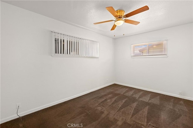 empty room featuring ceiling fan, dark colored carpet, and baseboards
