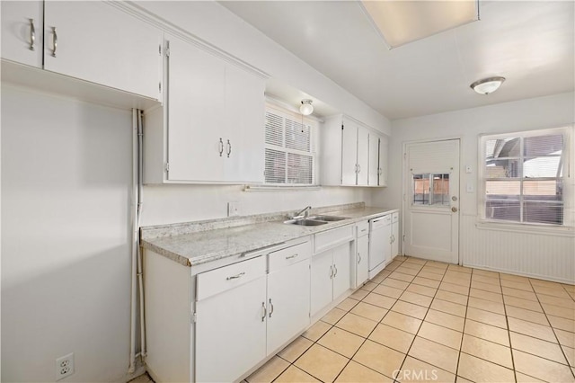 kitchen featuring light tile patterned flooring, a sink, white cabinetry, light countertops, and wainscoting