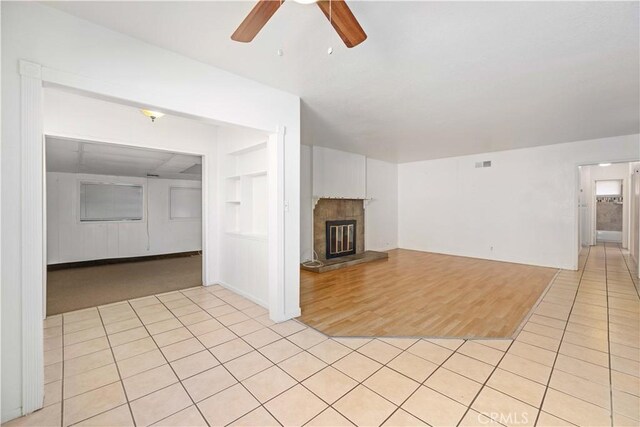 unfurnished living room featuring ceiling fan, a tiled fireplace, light tile patterned flooring, and built in features