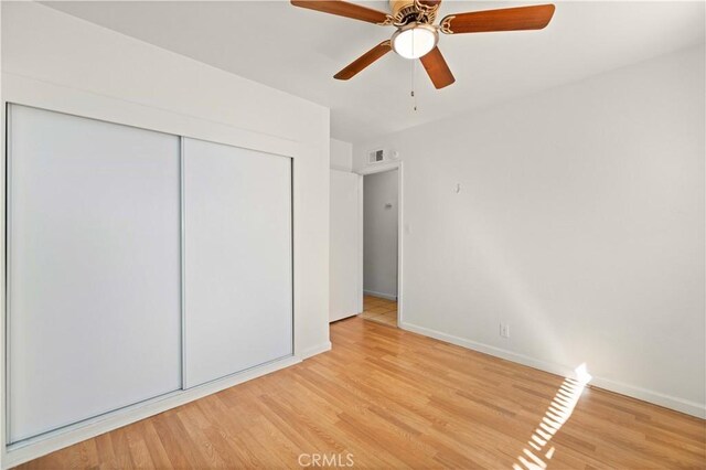 unfurnished bedroom with ceiling fan, light wood-type flooring, and a closet