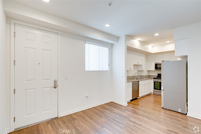 kitchen featuring light wood-type flooring, white cabinetry, appliances with stainless steel finishes, and light stone countertops