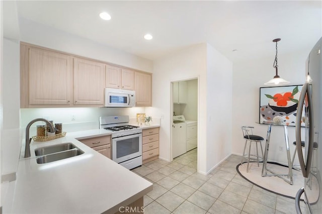 kitchen featuring washer and dryer, light brown cabinets, decorative light fixtures, white appliances, and sink