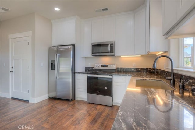 kitchen with dark stone countertops, appliances with stainless steel finishes, dark hardwood / wood-style flooring, white cabinets, and sink