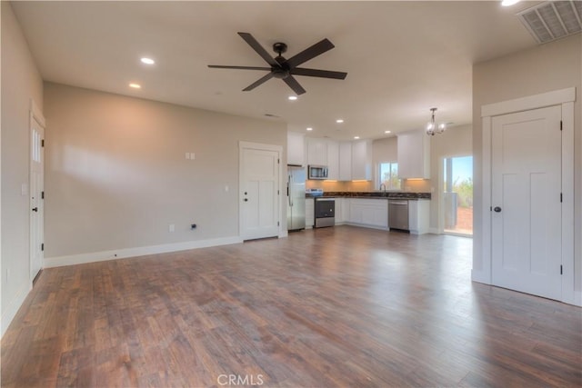 unfurnished living room with ceiling fan with notable chandelier, dark wood-type flooring, and sink