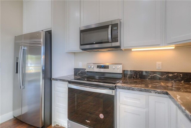 kitchen with stainless steel appliances, white cabinetry, dark stone countertops, and dark wood-type flooring