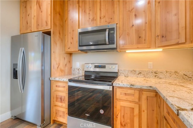 kitchen with light brown cabinetry, light stone counters, and appliances with stainless steel finishes