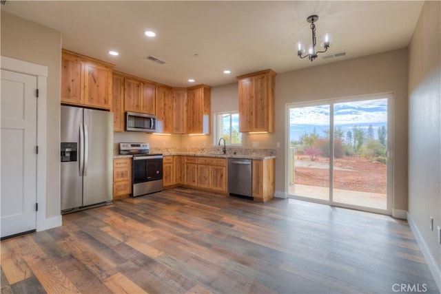 kitchen with stainless steel appliances, light stone countertops, dark hardwood / wood-style flooring, pendant lighting, and a notable chandelier