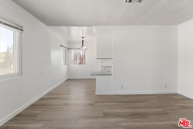 spare room with a textured ceiling, a healthy amount of sunlight, crown molding, and hardwood / wood-style floors