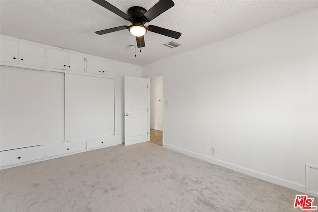 unfurnished bedroom featuring ceiling fan, light carpet, and a textured ceiling