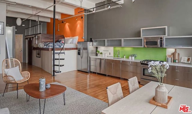 kitchen featuring light wood-type flooring, stainless steel appliances, sink, beamed ceiling, and a high ceiling