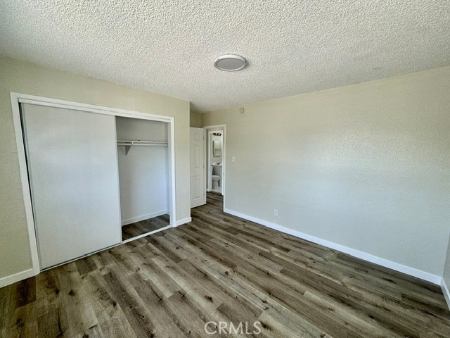 unfurnished bedroom with a textured ceiling, dark wood-type flooring, and a closet