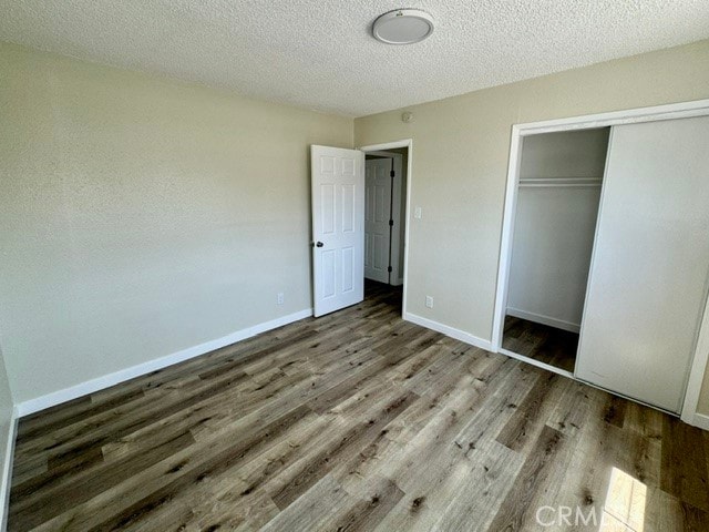 unfurnished bedroom featuring a textured ceiling, wood-type flooring, and a closet