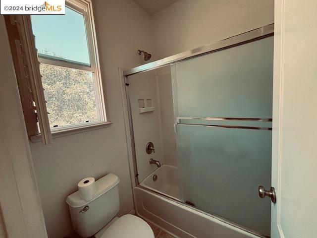 bathroom featuring combined bath / shower with glass door and toilet