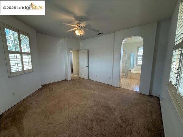 unfurnished bedroom featuring ceiling fan, carpet, multiple windows, and ensuite bath