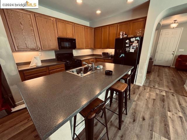 kitchen with black appliances, an island with sink, sink, and hardwood / wood-style floors