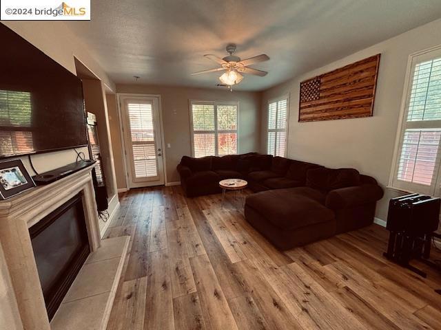 living room with ceiling fan, a tiled fireplace, plenty of natural light, and light hardwood / wood-style flooring