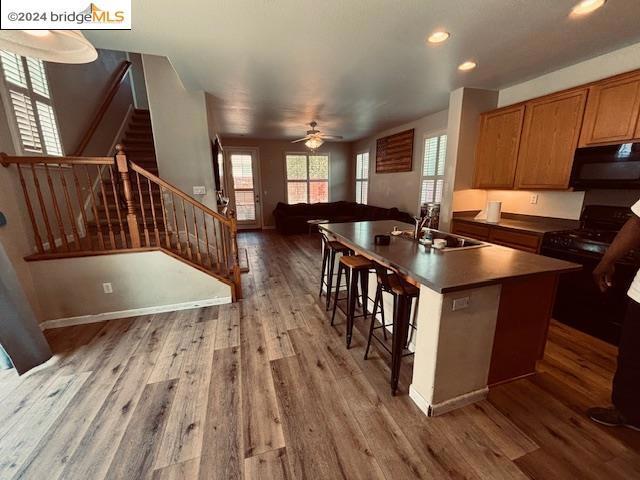 kitchen with ceiling fan, hardwood / wood-style floors, black appliances, sink, and a kitchen island with sink