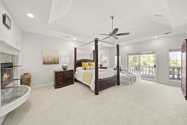 carpeted bedroom featuring access to exterior, a tray ceiling, a fireplace, and ceiling fan