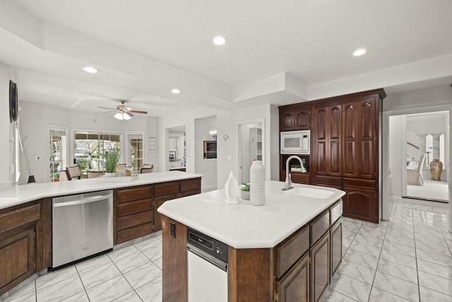 kitchen featuring white microwave, a center island with sink, ceiling fan, dishwasher, and sink