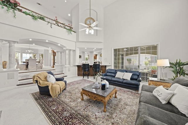 living room featuring carpet, decorative columns, a high ceiling, and ceiling fan with notable chandelier