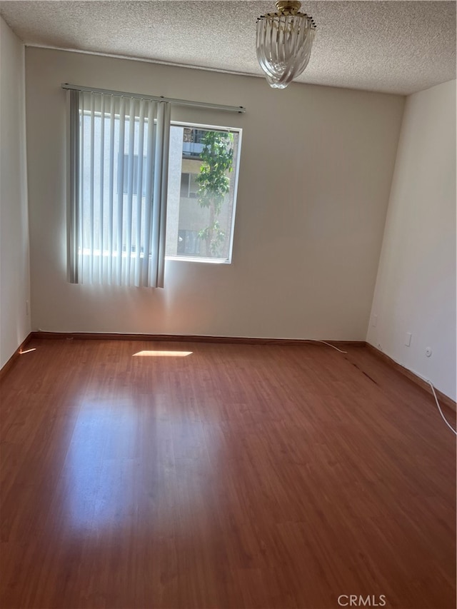 spare room with an inviting chandelier, a textured ceiling, and hardwood / wood-style floors