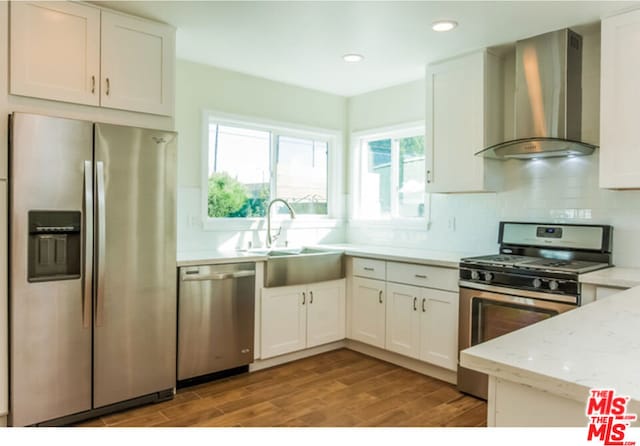 kitchen with white cabinets, light hardwood / wood-style flooring, wall chimney exhaust hood, light stone counters, and stainless steel appliances