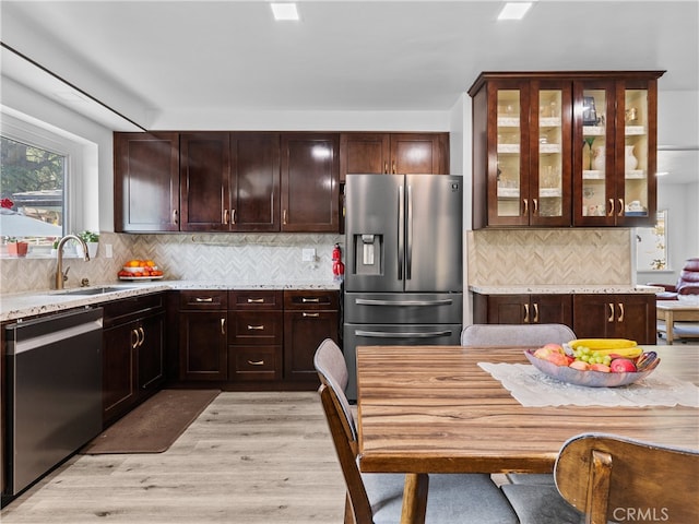 kitchen with decorative backsplash, appliances with stainless steel finishes, light stone countertops, light wood-type flooring, and sink