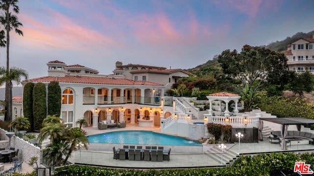 back house at dusk with an outdoor living space, a patio, a balcony, and a community pool