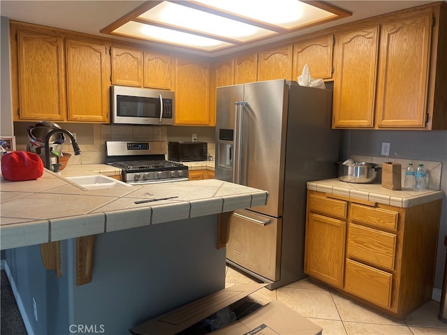 kitchen featuring light tile patterned floors, sink, kitchen peninsula, stainless steel appliances, and tile countertops