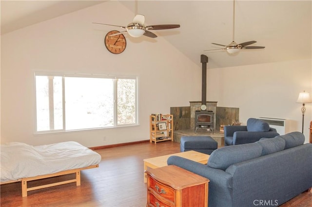 living room featuring ceiling fan, high vaulted ceiling, a wood stove, and dark hardwood / wood-style flooring