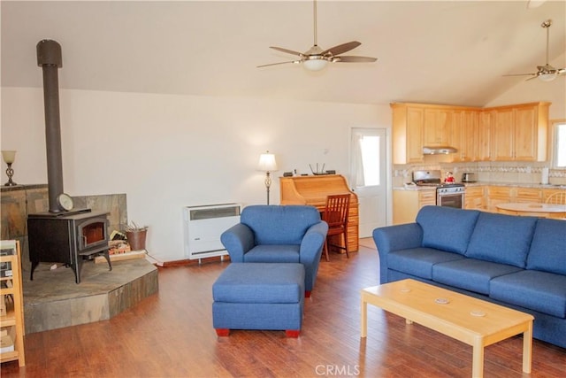 living room with ceiling fan, heating unit, dark hardwood / wood-style flooring, vaulted ceiling, and a wood stove