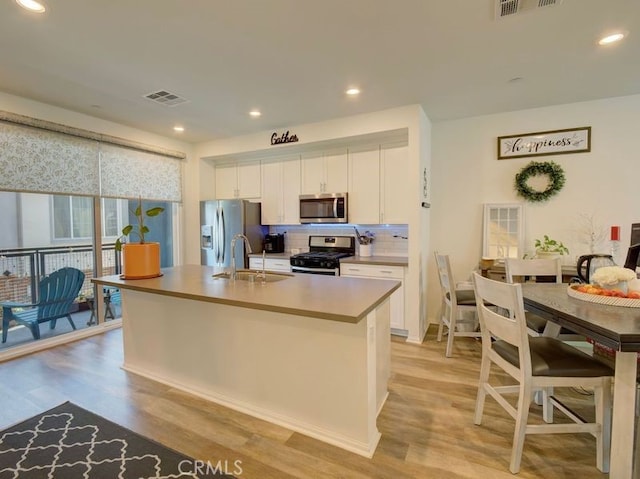 kitchen with a kitchen island with sink, sink, light hardwood / wood-style floors, white cabinetry, and stainless steel appliances