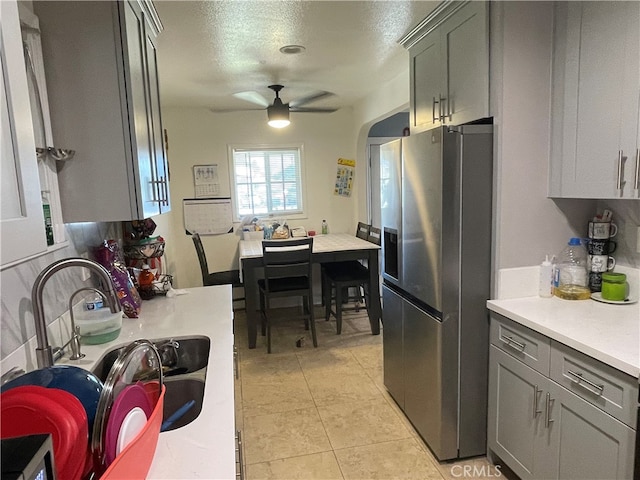 kitchen with stainless steel fridge, gray cabinets, a textured ceiling, ceiling fan, and sink