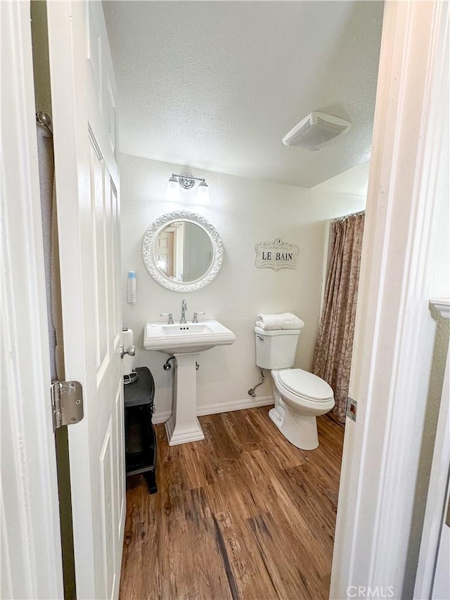 bathroom with toilet, wood finished floors, baseboards, and a textured ceiling