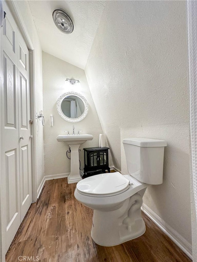 half bath with toilet, a textured ceiling, wood finished floors, baseboards, and a textured wall