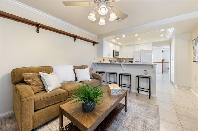 living room featuring a raised ceiling, light tile patterned floors, ceiling fan, ornamental molding, and sink